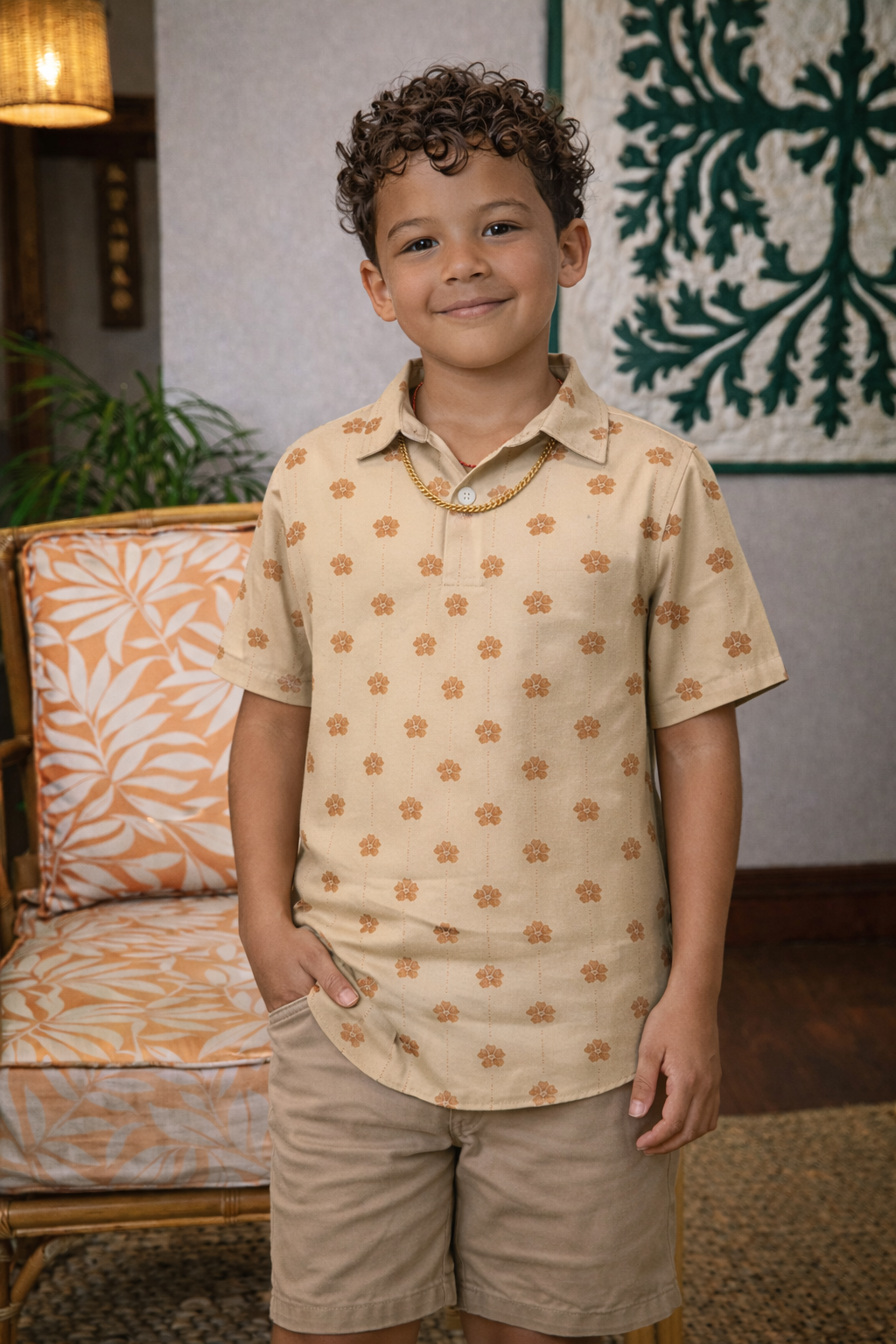 Child wearing a patterned shirt and shorts standing in a room with a couch and decorative wall.